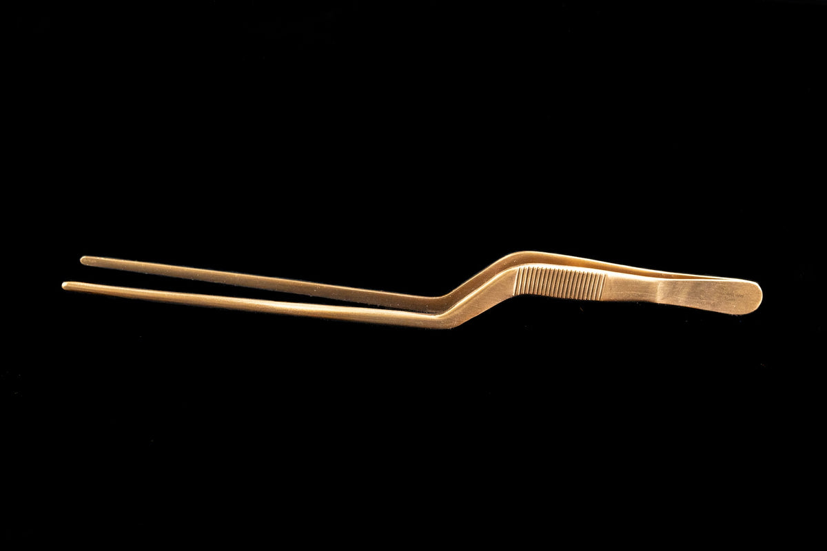 Pink gold offset plating tweezers with angled precision tips and textured ergonomic grip displayed against a black background for arranging delicate garnishes