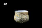 Handmade rounded glass cup with swirling cream, olive green, blue, and amber colors, textured flowing pattern, and a gently flared rim on a black background