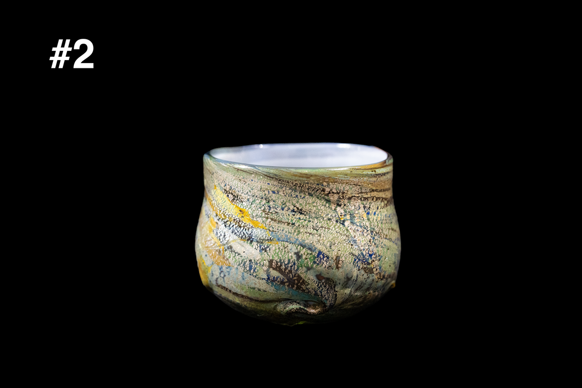 Handmade rounded glass cup with swirling cream, olive green, blue, and amber colors, textured flowing pattern, and a gently flared rim on a black background