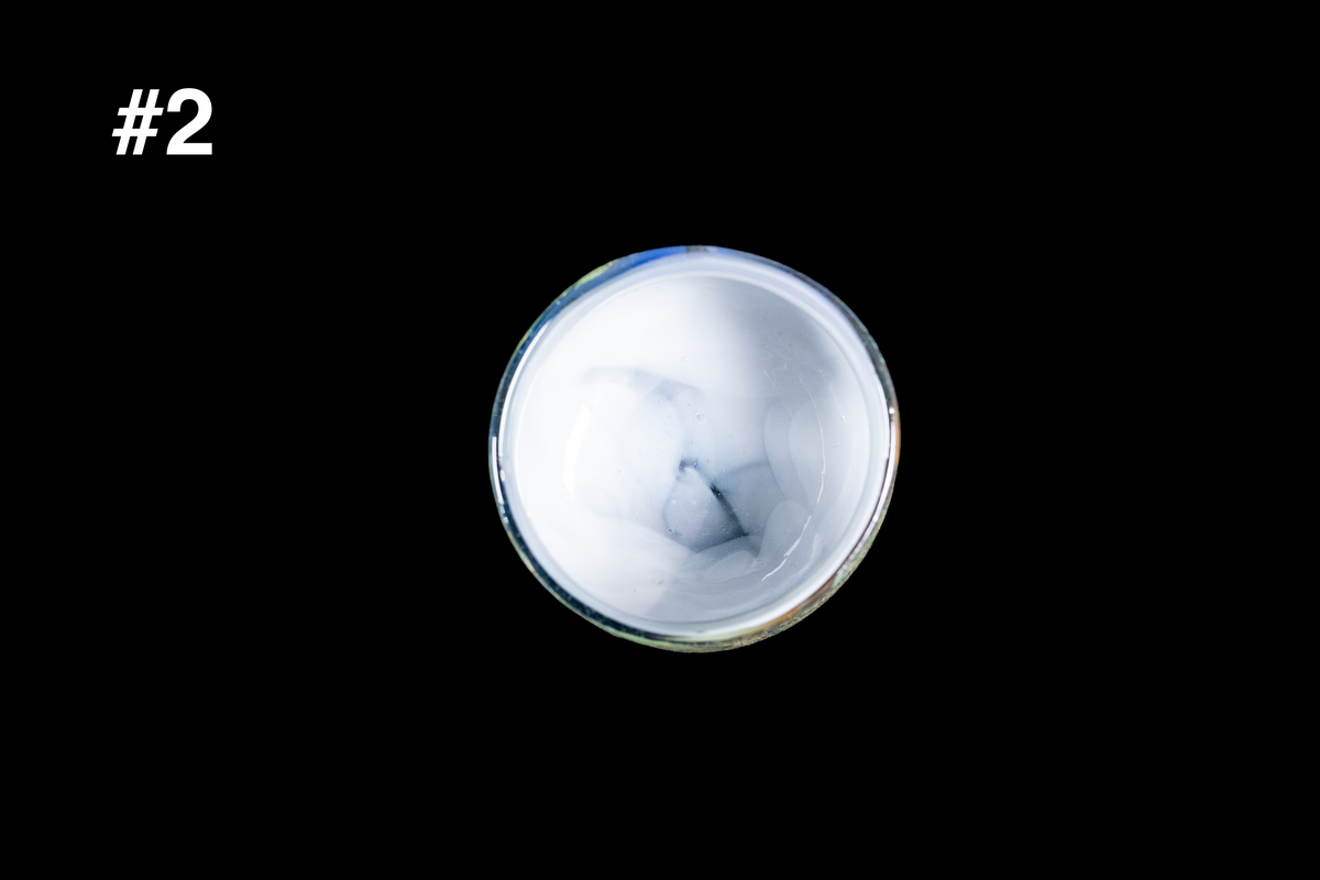 Top view of a handmade glass cup with a milky white interior, soft gray swirls, and a softly rounded rim against a black background