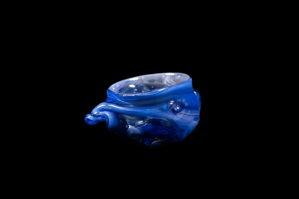 Handmade cobalt blue glass vessel with an ocean inspired rippled form and rounded opening displayed against a black background