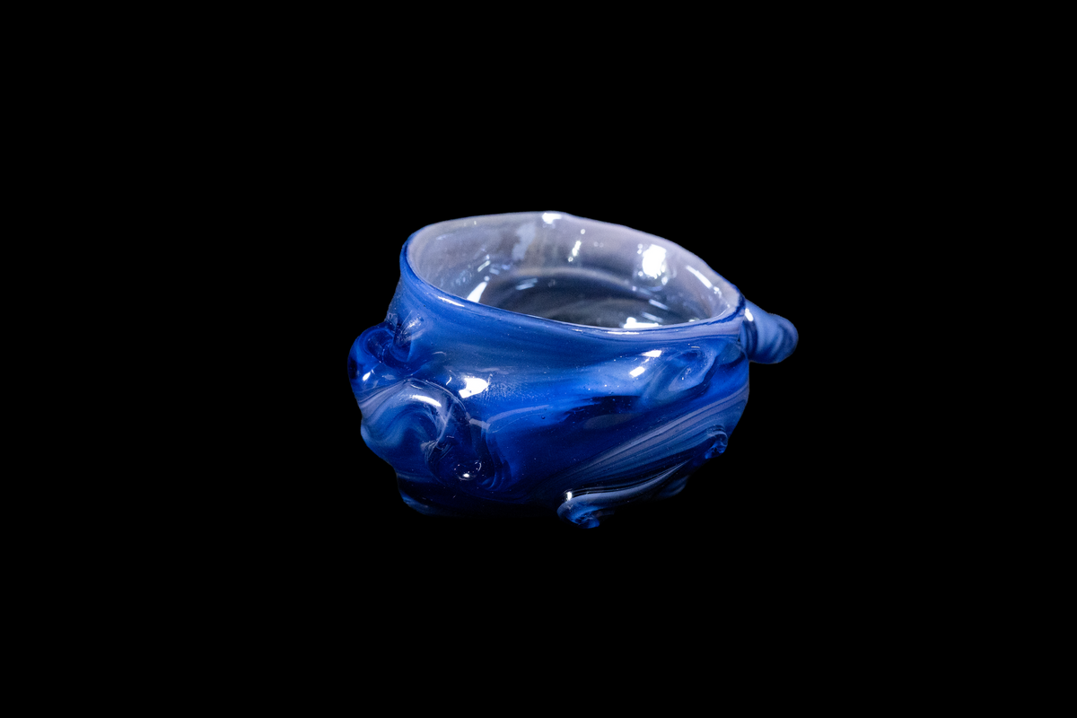 Handmade cobalt blue glass vessel with an irregular sculpted form, rounded textured sides, and a clear open rim displayed against a black background