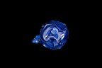 Bottom view of a handmade cobalt blue glass vessel with white swirls and a curled tail-like projection against a black background
