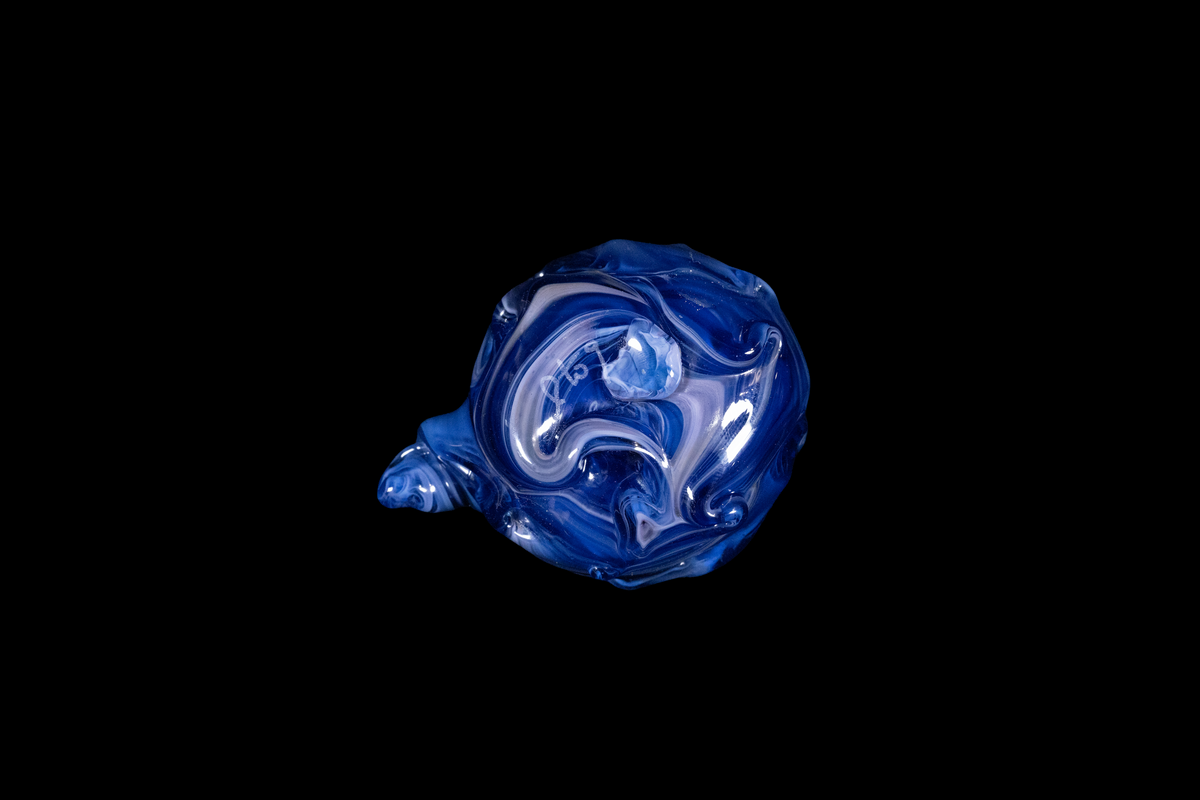 Bottom view of a handmade cobalt blue glass vessel with white swirls and a curled tail-like projection against a black background