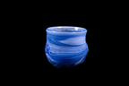 Handmade blue glass cup with layered flowing swirls, rounded sides, and a gently flared rim against a black background