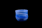 Blue purple handmade glass cup with layered flowing swirls, rounded shape, and a gently uneven rim displayed against a black background
