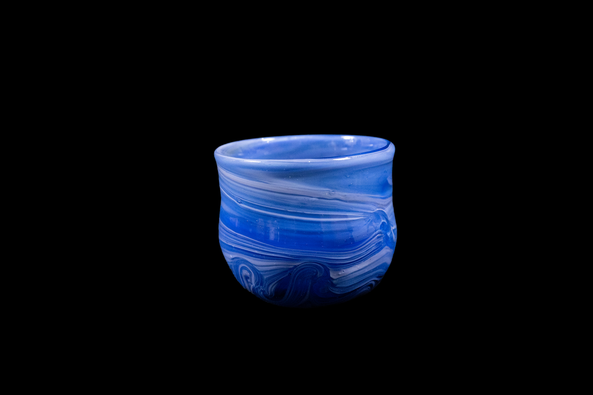 Blue purple handmade glass cup with layered flowing swirls, rounded shape, and a gently uneven rim displayed against a black background