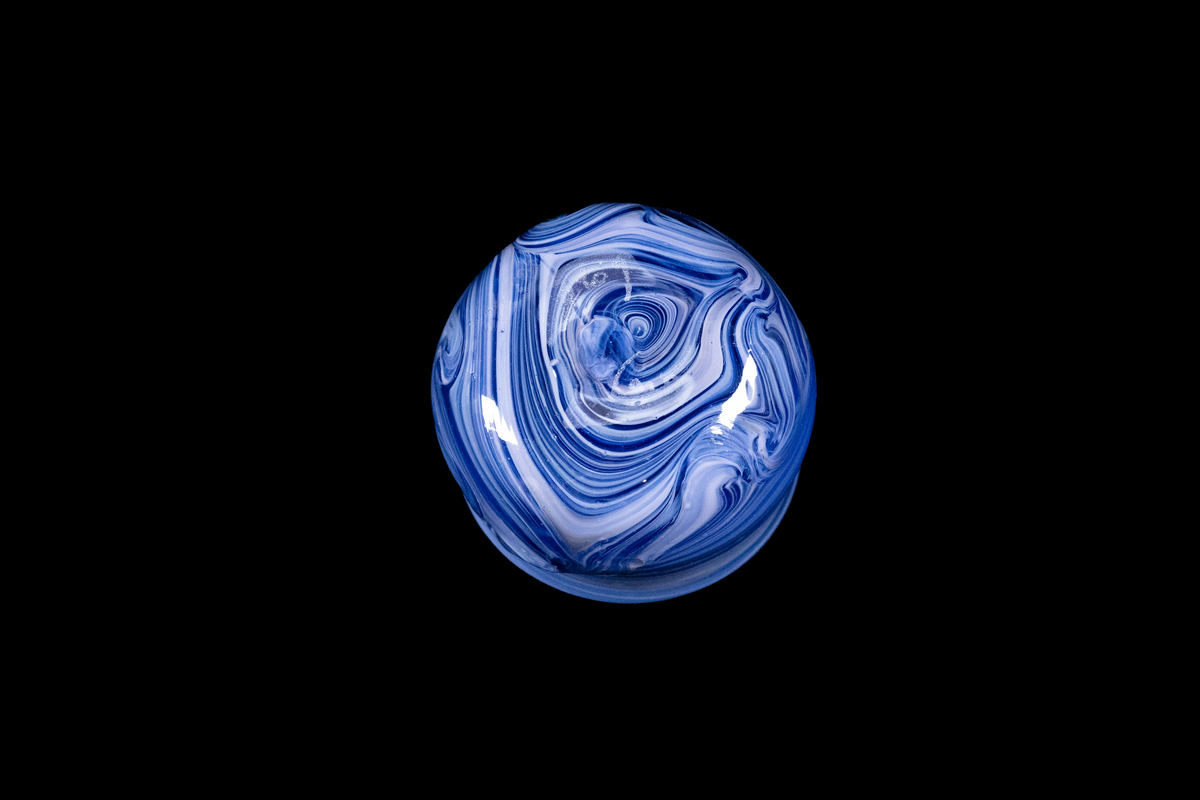 Bottom view of a handmade blue and white glass cup with intricate flowing swirls and a rounded shape against a black background