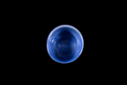 Top view of a deep blue glass cup with a rounded rim and flowing swirls visible through the bowl against a black background