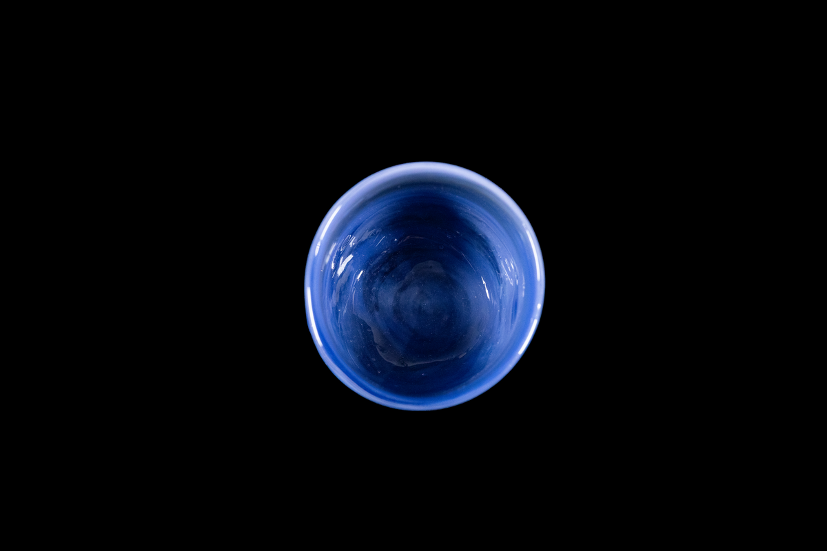 Top view of a deep blue glass cup with a rounded rim and flowing swirls visible through the bowl against a black background