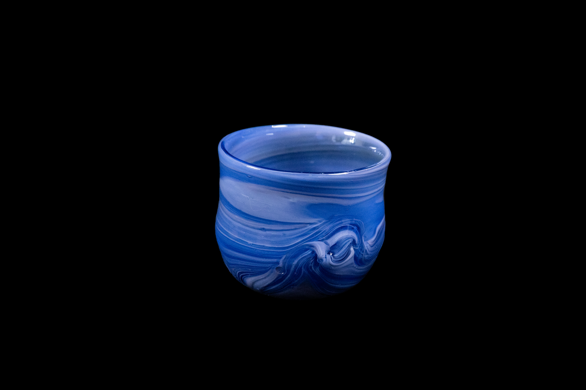 Handmade blue glass tumbler with flowing cobalt and violet swirls and a softly rounded rim against a black background