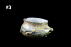 Handmade glass drinking cup with a flared rim and swirling silver, blue, and gold textures against a black background