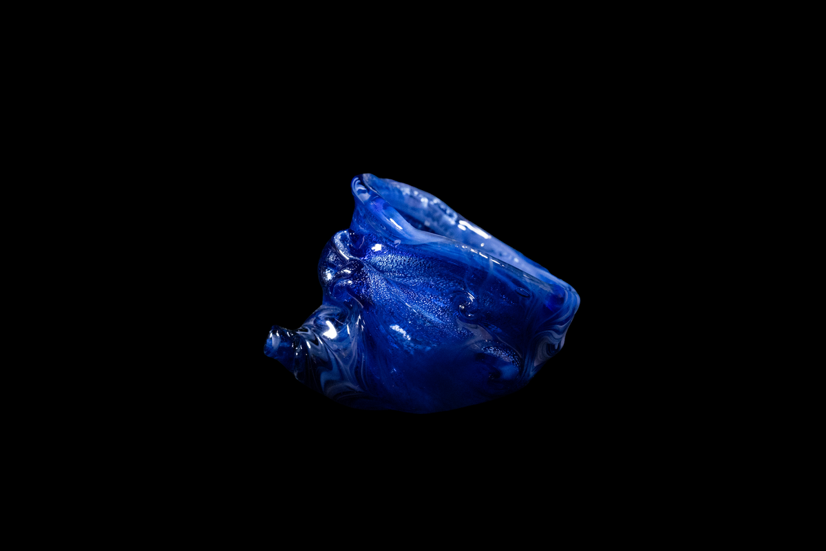 Handmade cobalt blue glass vessel with an organic, sculpted form, rippled surface, and uneven opening against a black background