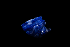 Sculptural cobalt blue handmade glass vessel with swirling wave-like ridges and glossy highlights against a black background