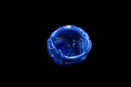 Deep blue handmade glass vessel viewed from above with a rounded wavy rim and textured interior against a black background