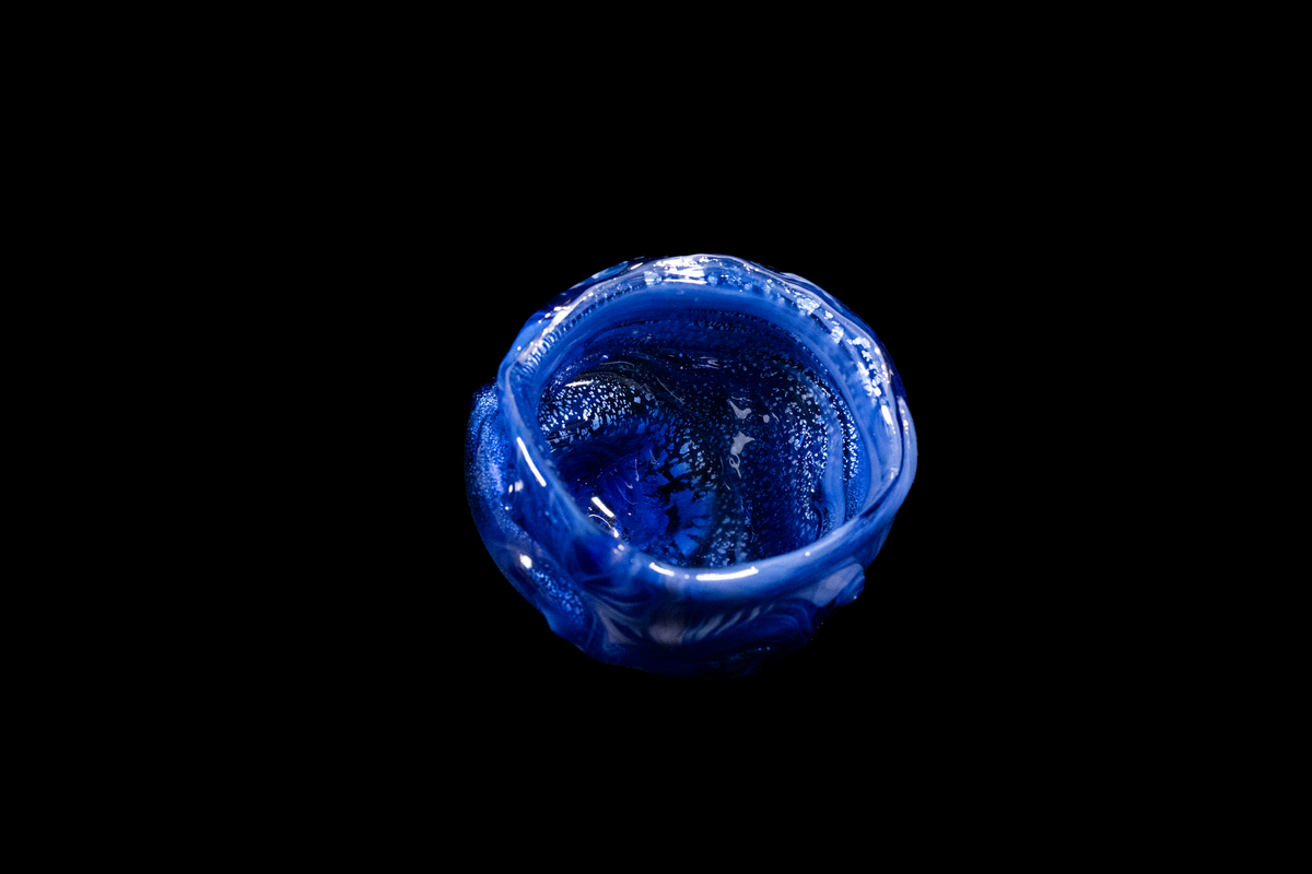 Deep blue handmade glass vessel viewed from above with a rounded wavy rim and textured interior against a black background