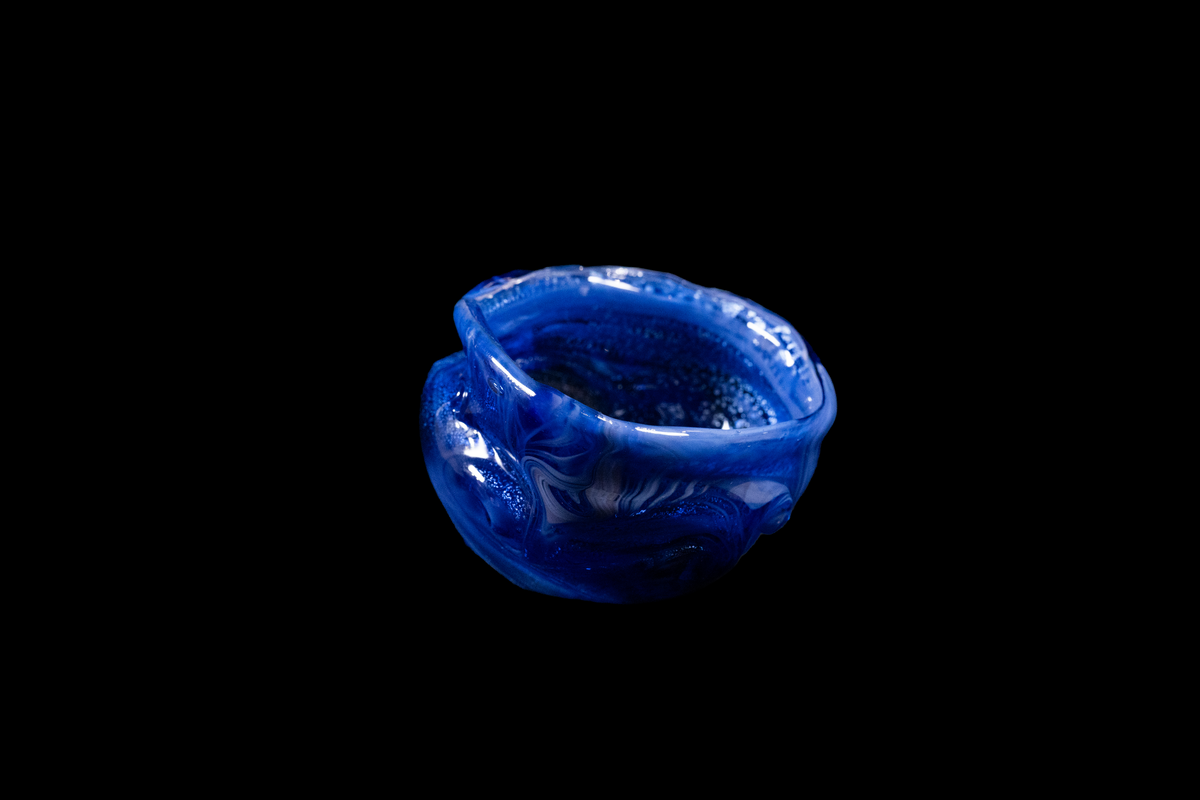 Handmade cobalt blue glass vessel with a rounded opening, rippled sculptural sides, and glossy textured swirls displayed against a black background