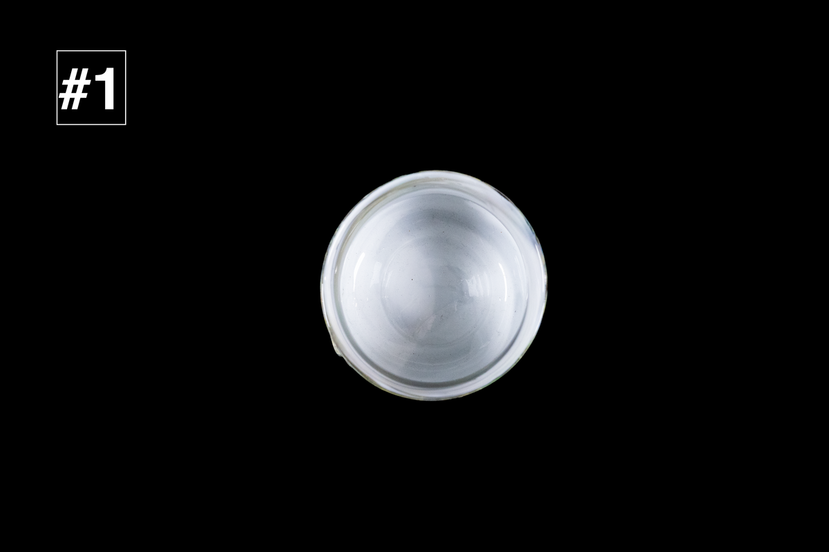 Top view of a handmade glass cup with a milky white interior and softly rounded rim against a black background