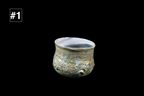 Small handmade glass drinking cup with a rounded shape, rippled multicolored texture, and pale blue curved rim against a black background