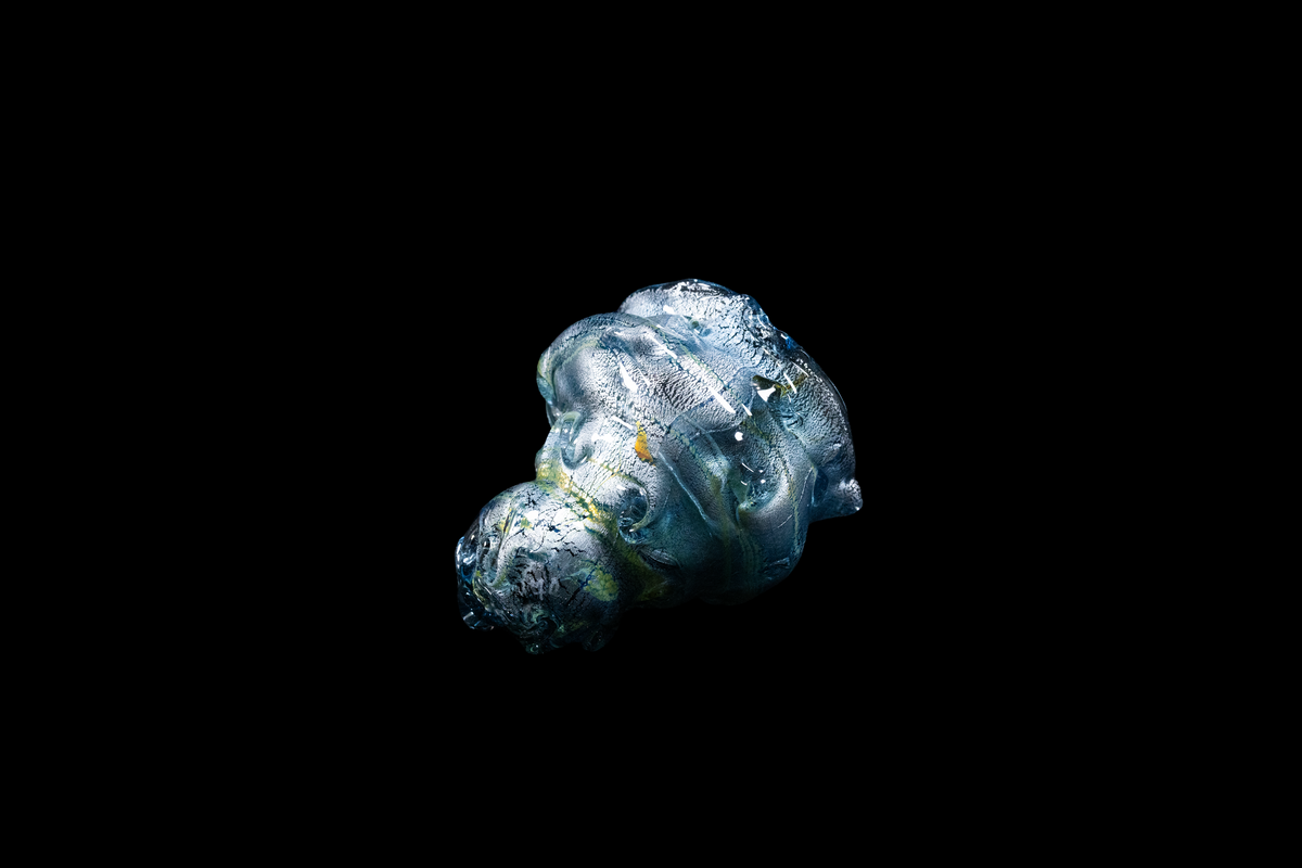 Handmade blue silver glass cup with flowing sculptural ridges and sparkling textured details displayed against a black background