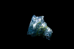 Handmade blue and silver glass cup with flowing sculptural contours and textured highlights isolated against a black background
