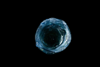 Top view of a handmade blue glass cup with a rugged wavy rim and deep translucent center against a black background