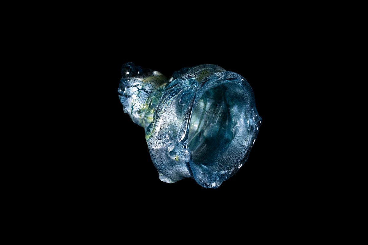 Handmade blue glass cup with silvery flowing swirls and an organic sculptural shape against a black background