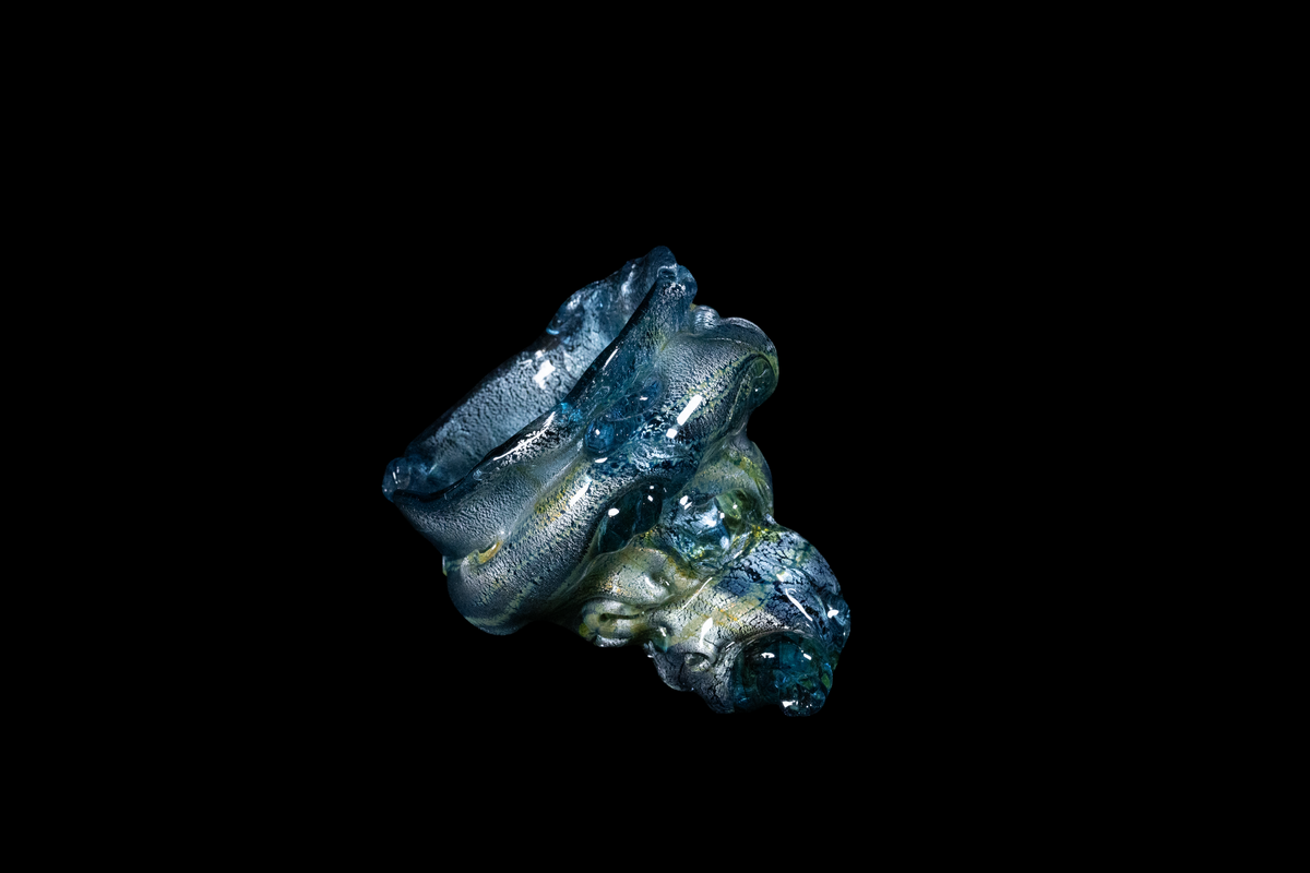 Handmade blue and silver glass vessel with dramatic flowing folds and a sculptural ocean-inspired form against a black background