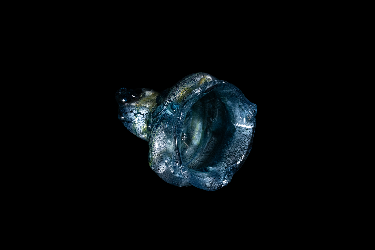 Sculptural blue and silver handmade glass cup with layered flowing contours and textured details displayed against a black background