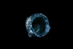 Top view of a handmade blue glass cup with a rugged asymmetrical rim and deep swirling interior set against a black background