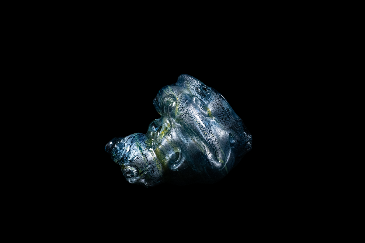 Handmade silver blue glass cup with layered flowing ridges and a rounded sculptural form against a black background