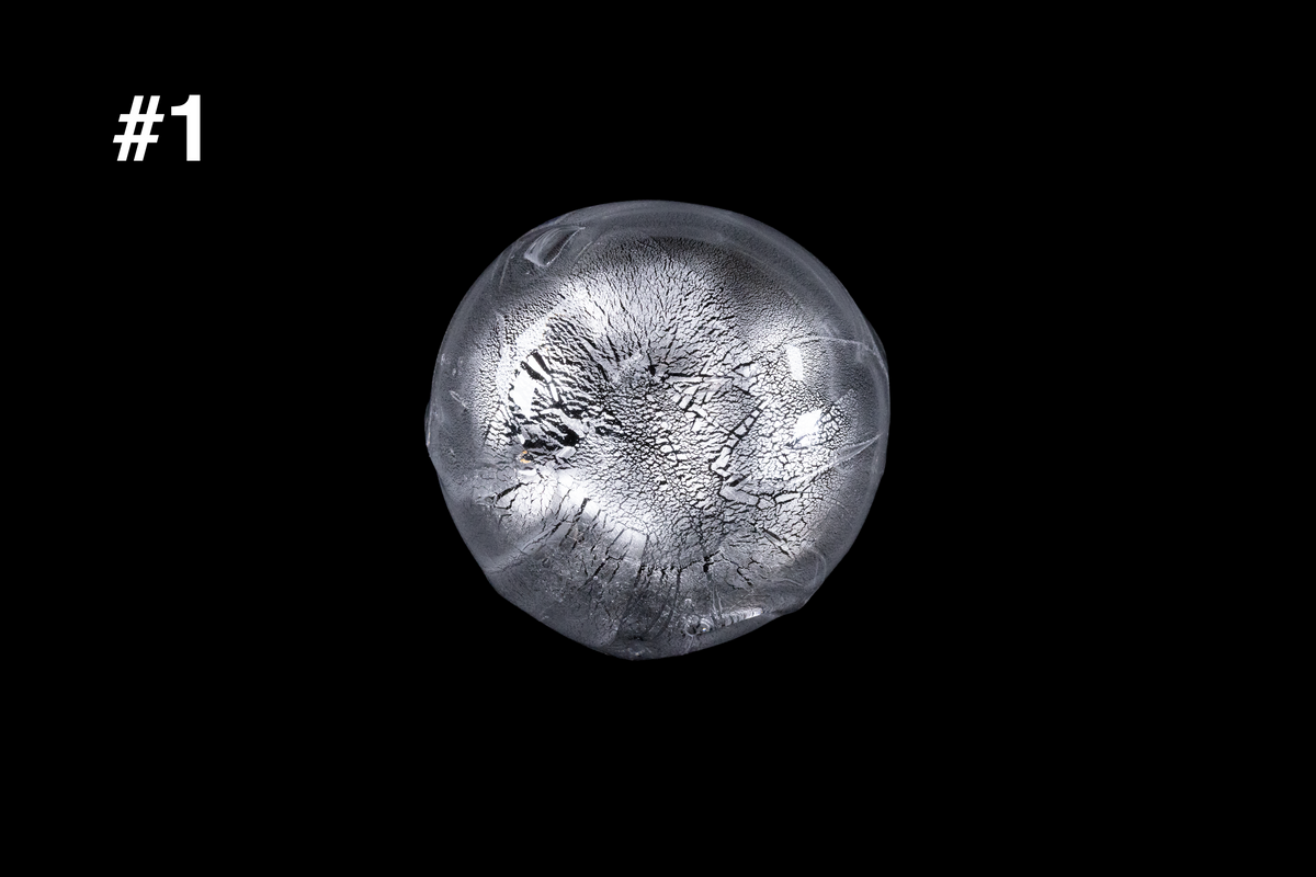 Top view of a handmade silver toned glass sake cup with a rounded shape and intricate frosted crystalline texture against a black background