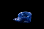Handmade cobalt blue glass vessel with a rounded bowl and a curled tail-like projection, marbled with pale lavender swirls, against a black background