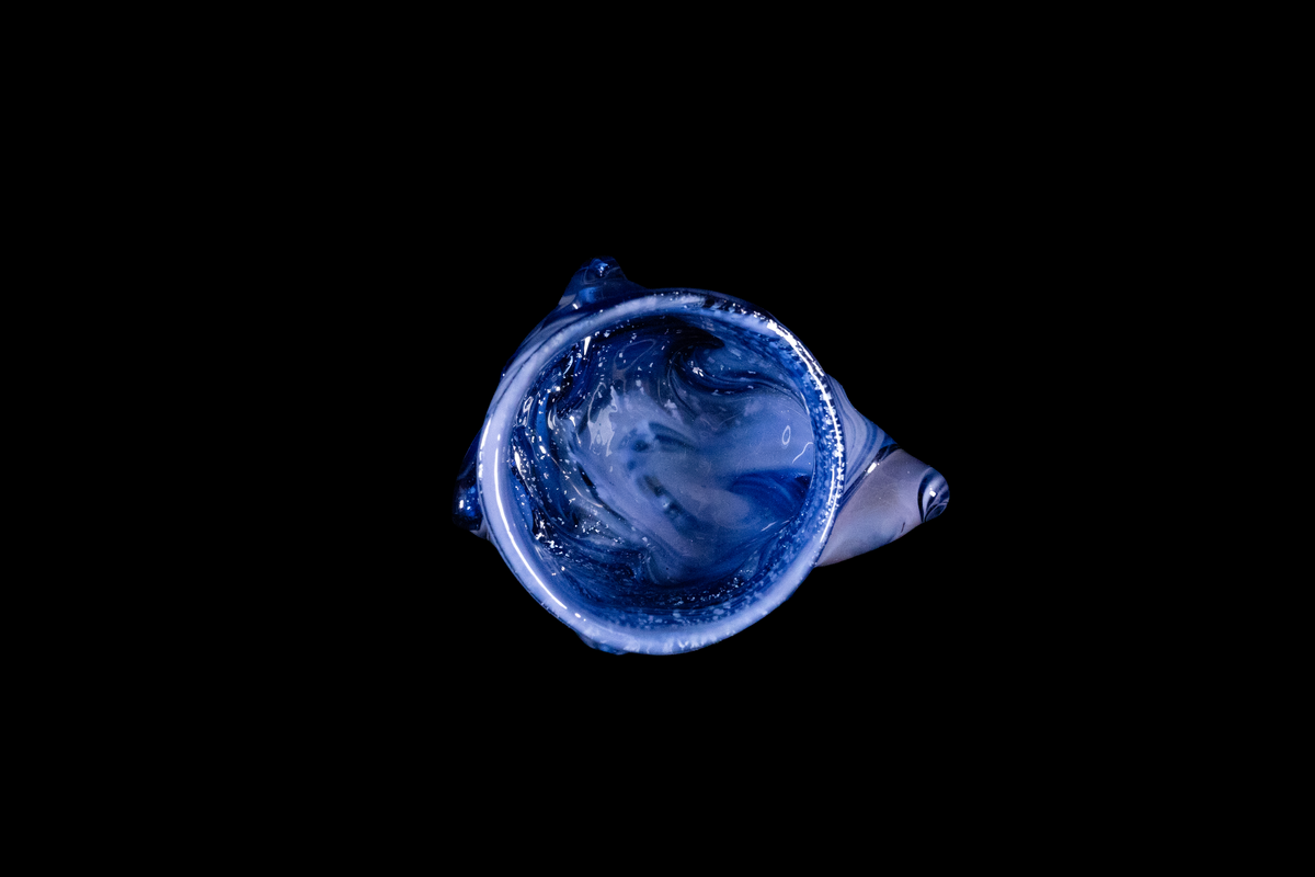 Top view of a handmade blue glass vessel with swirling translucent patterns and rounded side details against a black background