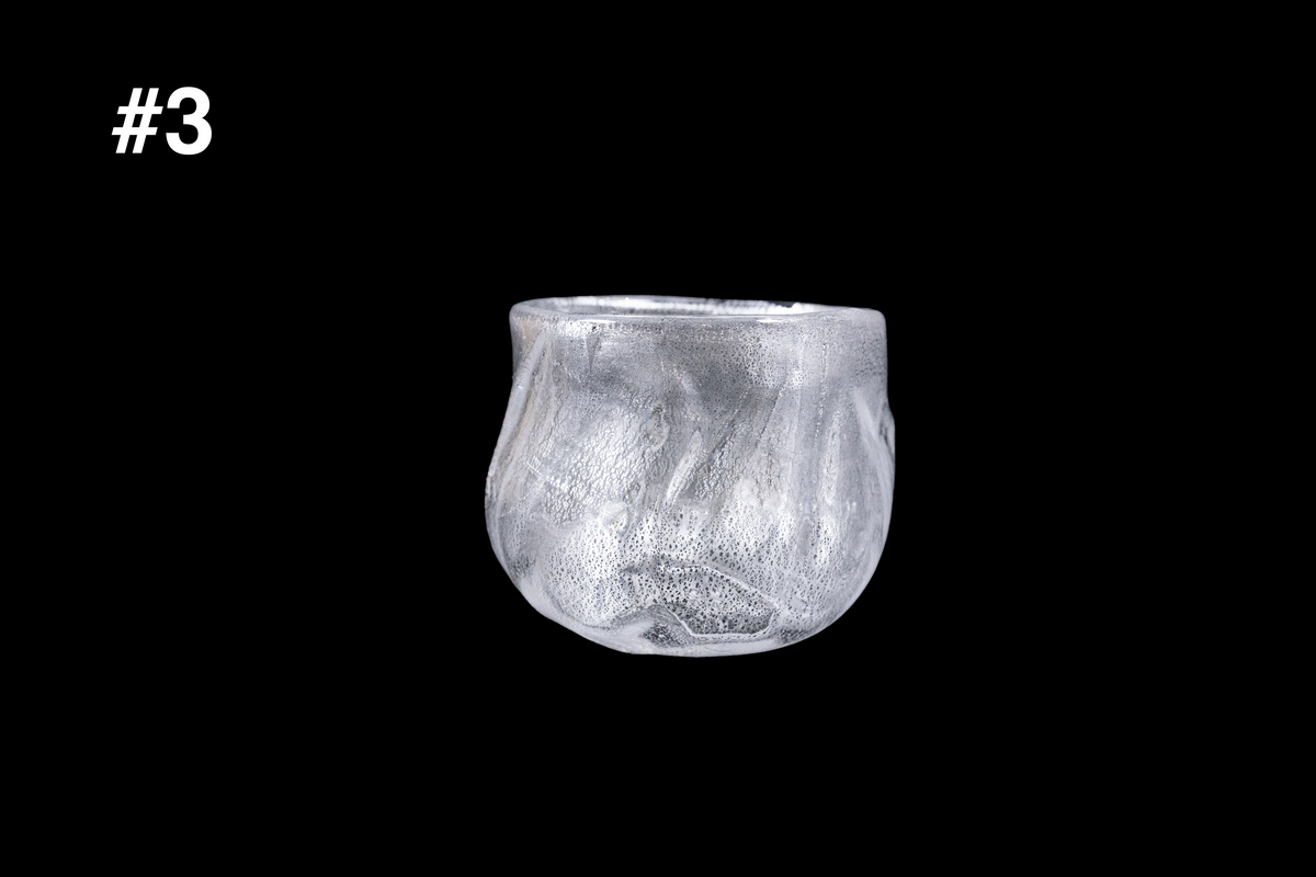 Silver-toned handmade glass guinomi cup with a rounded form and softly rippled textured surface against a black background