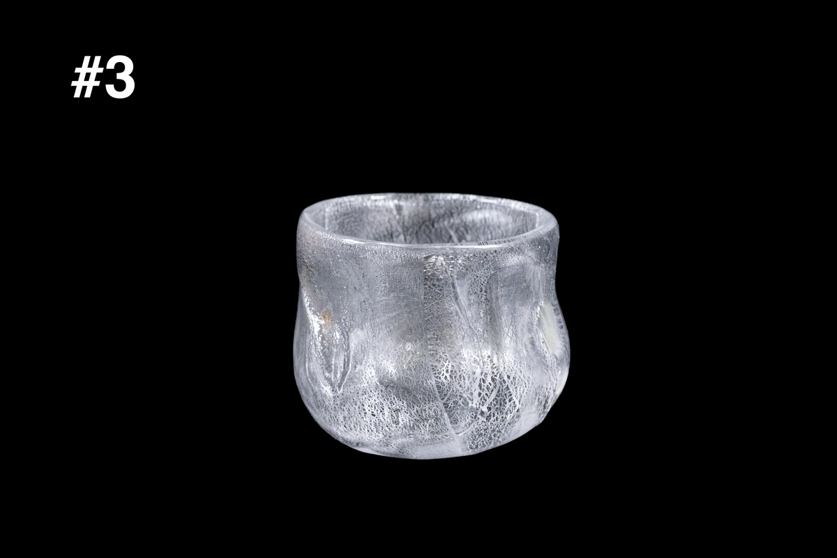Handmade frosted glass guinomi cup with a rounded shape and richly textured silver white surface against a black background