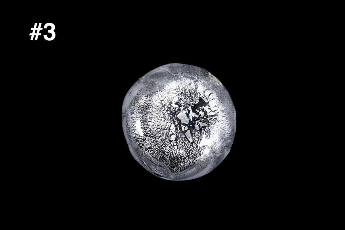 Silver toned handmade glass sake cup with a softly rounded shape and intricate rippled texture surrounding a dark organic center against a black background