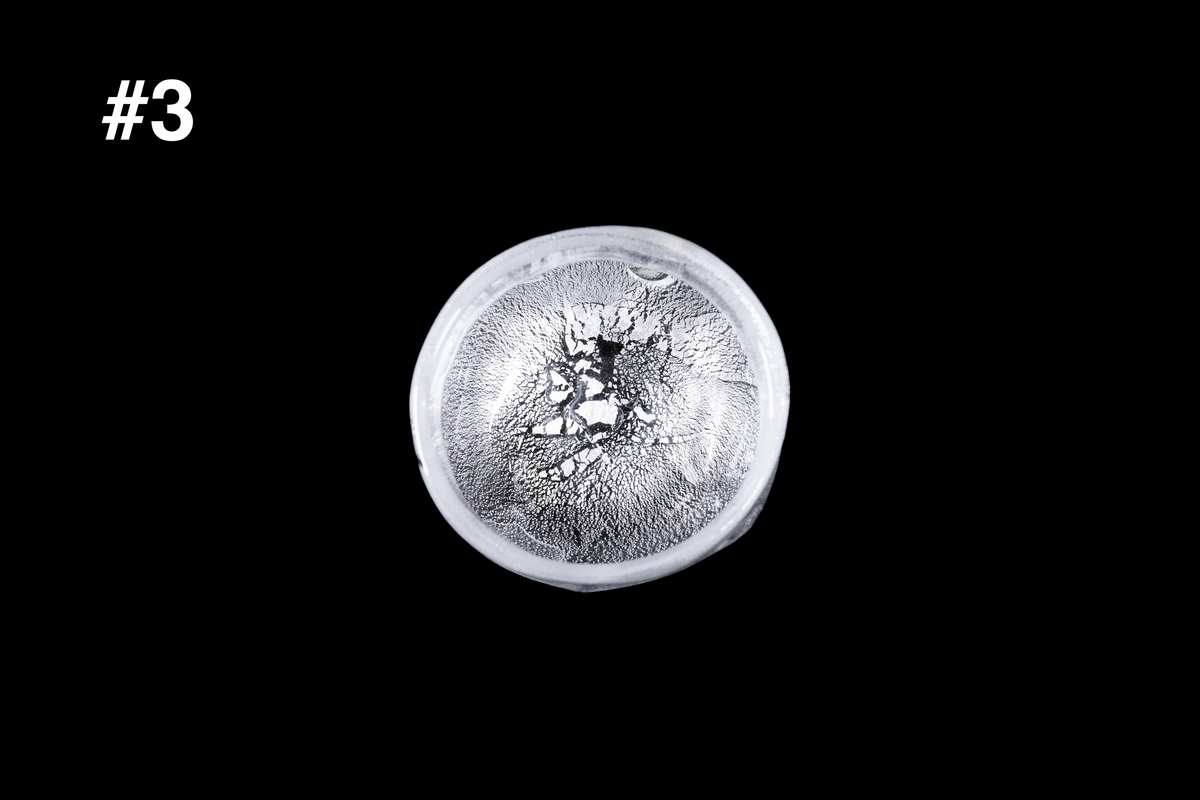 Small handmade silver toned guinomi glass cup viewed from above with a bright white silver finish and richly textured interior against a black background
