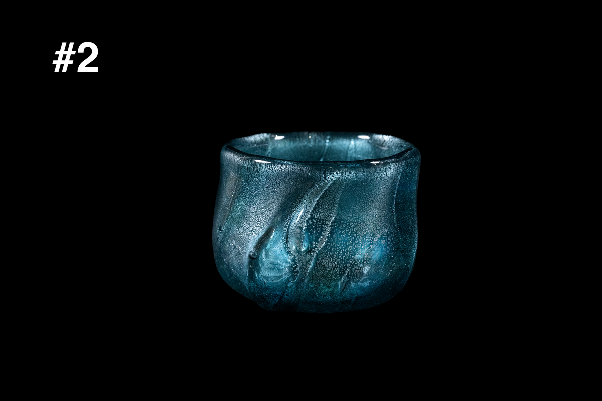 Handmade teal glass guinomi with silver leaf inclusions, a softly flared rim, and vertical sculpted ridges against a black background