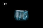 Handmade teal glass guinomi sake cup with shimmering silver leaf, an uneven rim, and a rounded shape against a black background