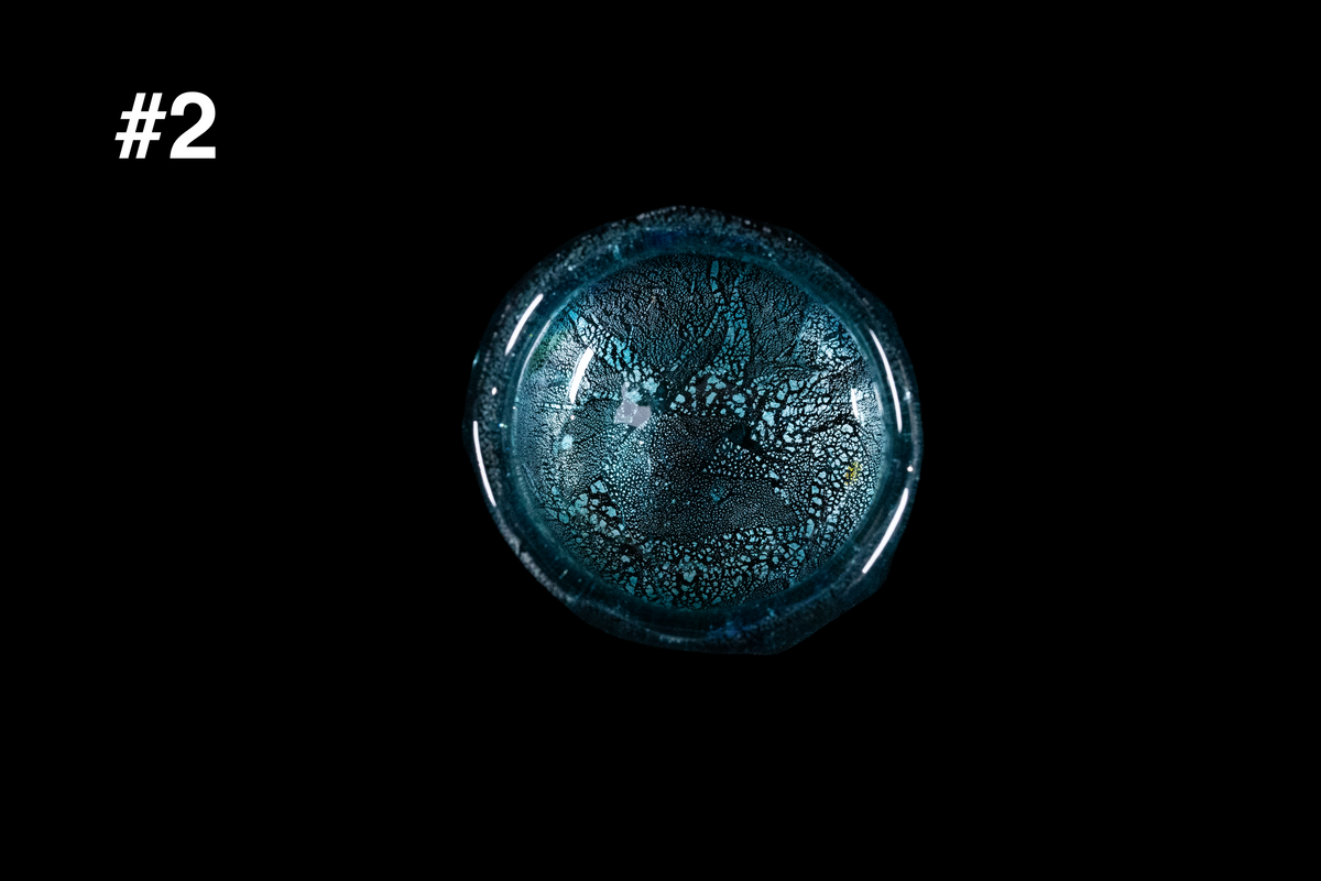 Top view of a handmade teal glass guinomi showing crackled silver leaf and small bubbles across the bottom against a black background