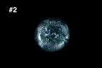 Bottom view of a handmade teal glass guinomi with crackled silver leaf and small bubbles against a black background