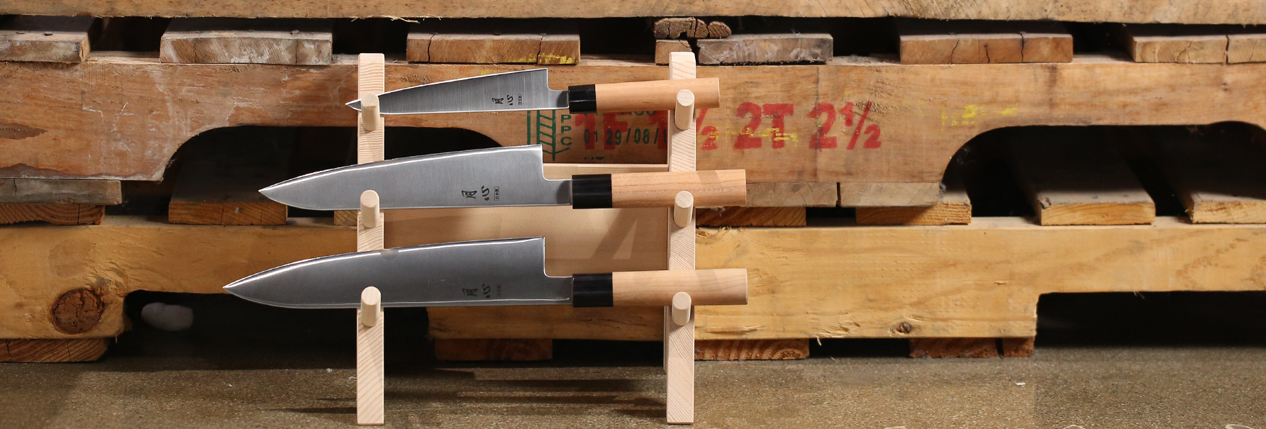 Set of knives displayed on a wooden stand against a wooden pallet background