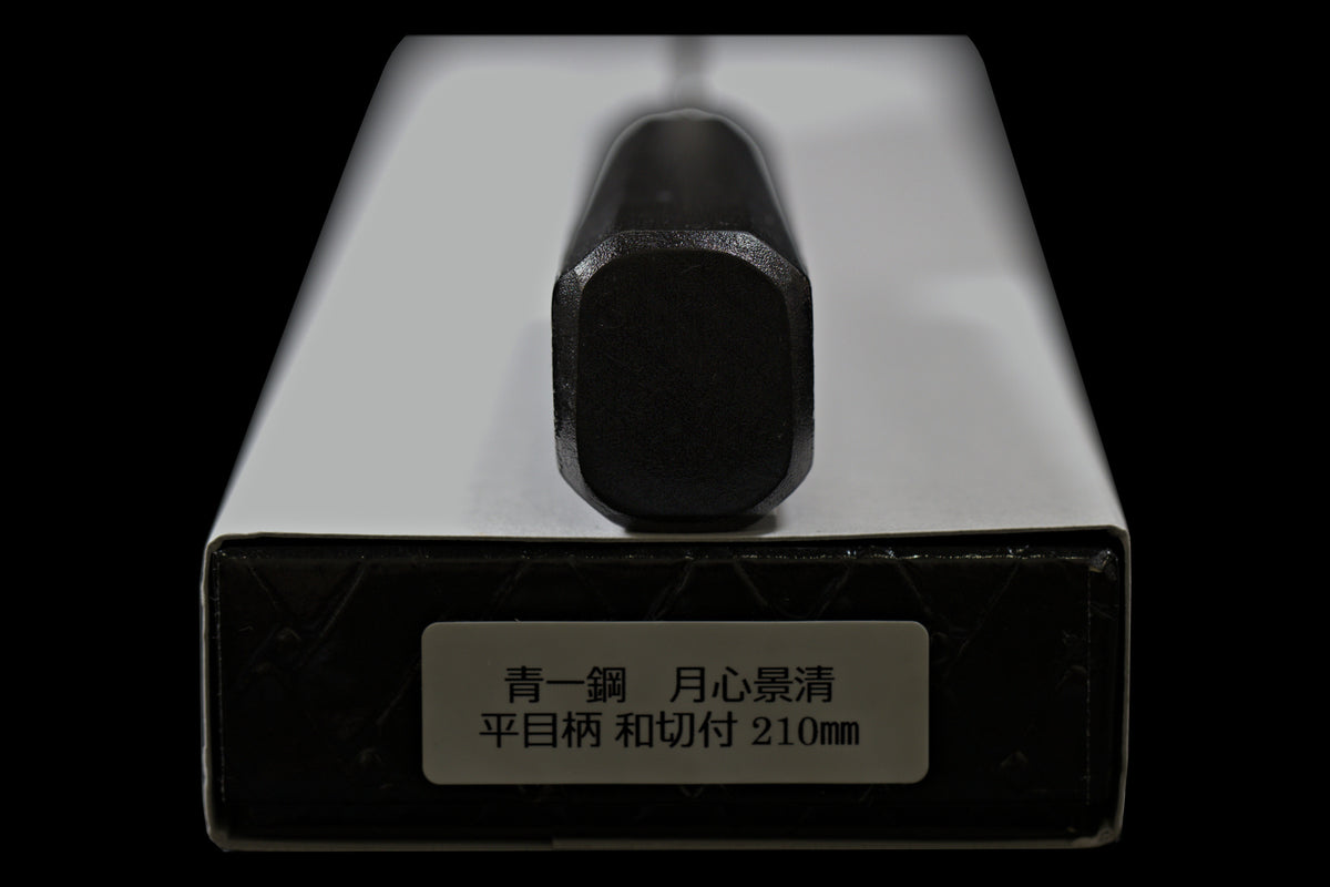 End of the black octagonal handle on the Gesshin Kagekiyo 210mm Blue #1 Kiritsuke Wa-Gyuto, resting on its box with label