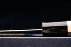 Close side view of the polished blade and octagonal ho wood handle of a Gesshin Ginga 210mm carbon wa gyuto by Ashi Hamono on a dark background