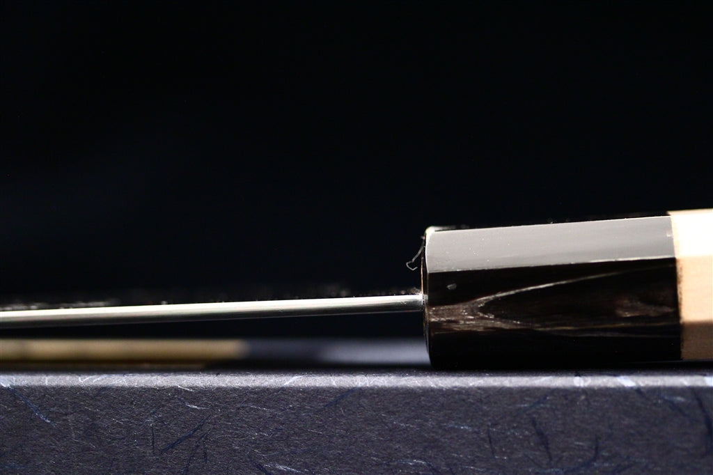 Close side view of the polished blade and octagonal ho wood handle of a Gesshin Ginga 210mm carbon wa gyuto by Ashi Hamono on a dark background