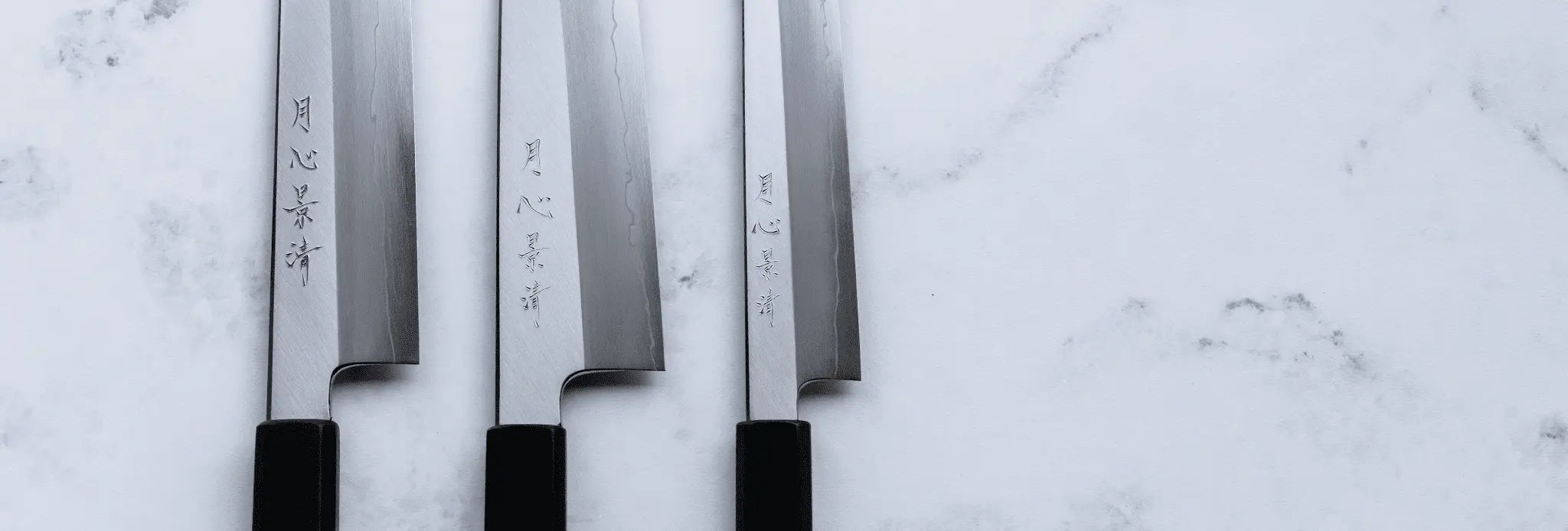 Three chef's knives with black handles on a light marble background