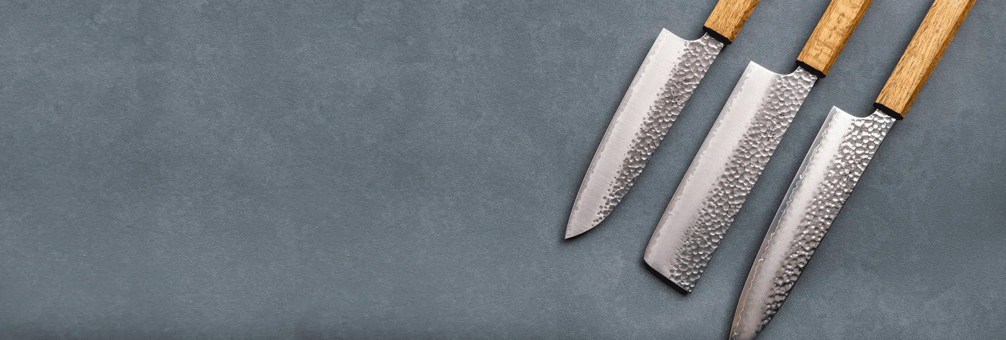 Three chef's knives with wooden handles on a gray background